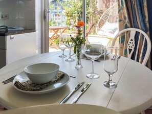 A dining table set with a bowl, plates, cutlery, and glasses, with a view of a garden and outdoor seating area.
