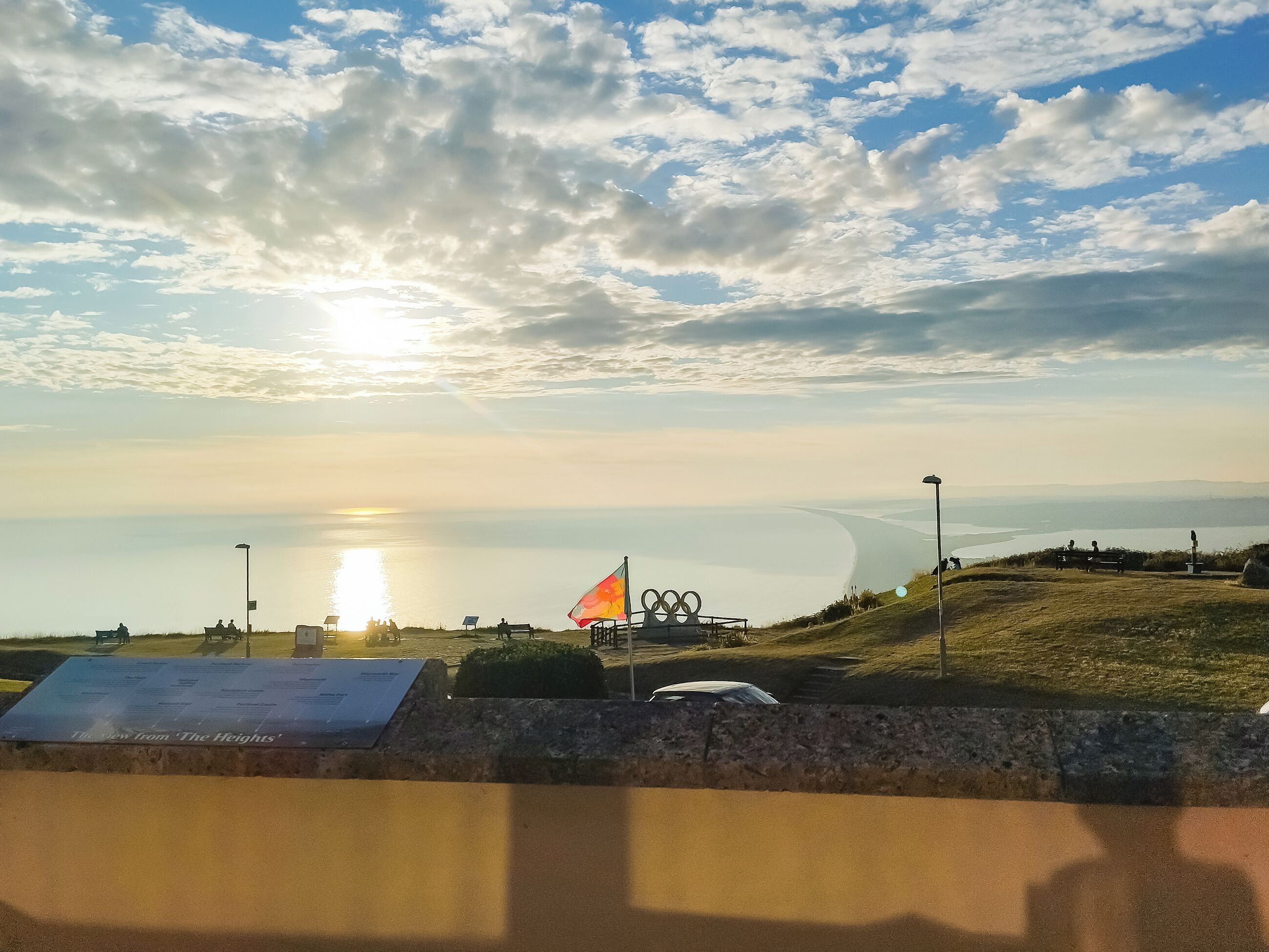 A coastal view with a sunset, a grassy area, and a sailboat.