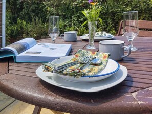 A table set with a plate, cutlery, a glass vase with flowers, a book, and a mug.