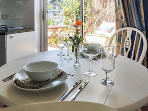 A dining table set with a bowl, plates, cutlery, and glasses, with a view of a garden and outdoor seating area.