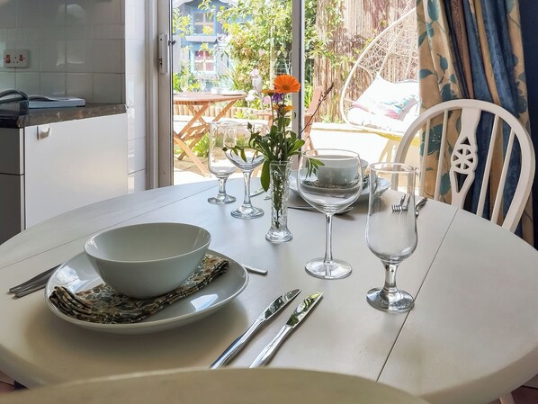 A dining table set with a bowl, plates, cutlery, and glasses, with a view of a garden and outdoor seating area.
