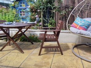 A patio with a wooden table and chairs, a hanging chair with a cushion, and a bamboo fence in the background.