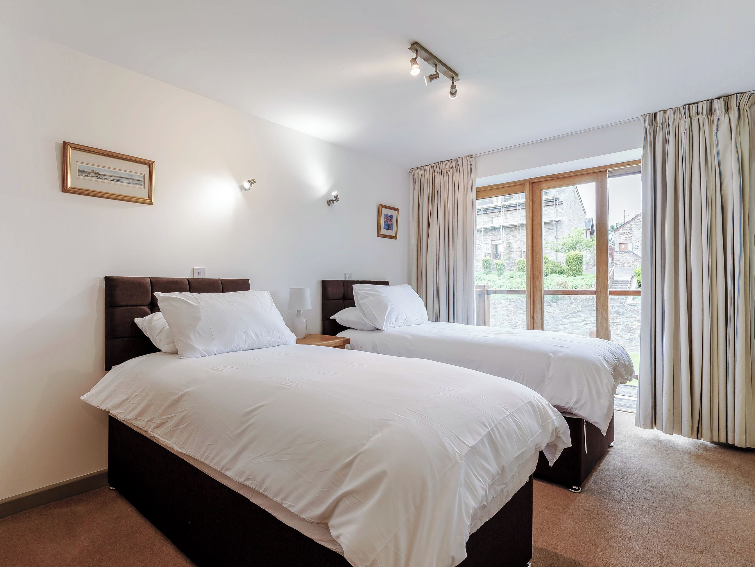 A hotel room with two beds, a window with curtains, a framed picture on the wall, and a ceiling light fixture.