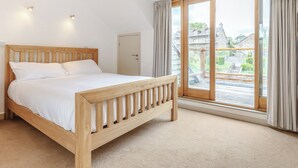 Een slaapkamer met een houten bed, een deur en een groot raam met gordijnen.