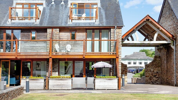 Een gebouw met twee verdiepingen, een balkon, grote ramen en een stenen gevel.