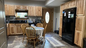 A kitchen with wooden cabinets, a black refrigerator, a dining table with chairs, and a window with a stained glass design. - 3 Dog Night (Vacation Rental) Private. 7 min to T.I.E.C (Mill Spring)