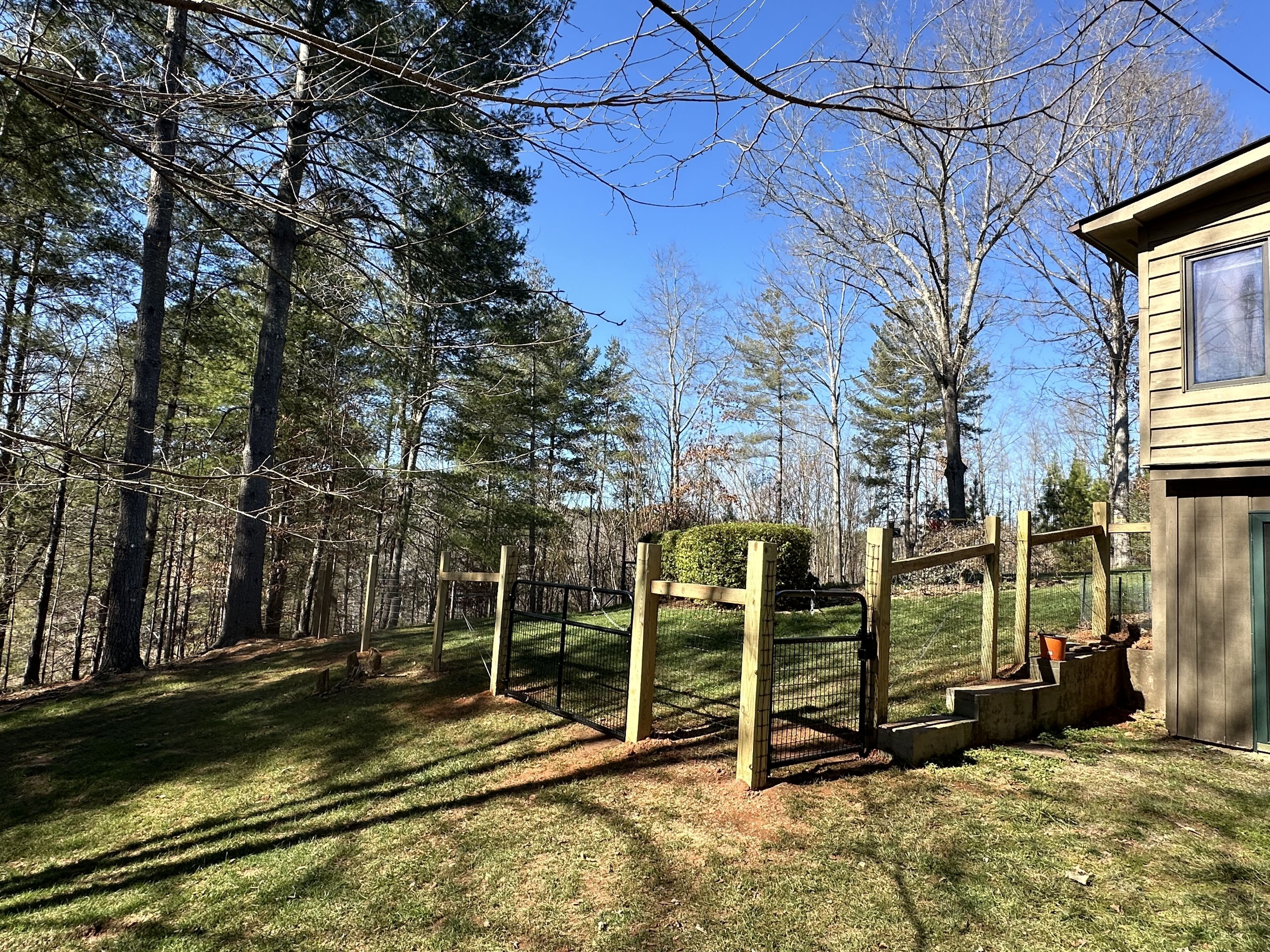A fenced outdoor area with a wooden structure, surrounded by trees and a clear sky.
