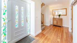 Ein Korridor mit Holzboden, einer grauen Tür mit Buntglas, einer Treppe und einem Holzschrank mit Spiegel und Blumenvasen.