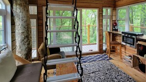 A wooden cabin interior with a loft bedroom, a dining area, and a kitchen. - One of a kind Treehouse on the Genesee River (BELFAST)