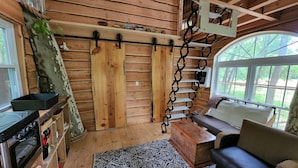 A cozy cabin interior with wooden walls, a kitchen area with a stove and oven, a dining table, and a sofa. - One of a kind Treehouse on the Genesee River (BELFAST)