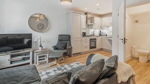 Un salon moderne doté d’un téléviseur à écran plat, d’un canapé confortable, d’un coin repas avec une table et d’une cuisine avec des meubles blancs et une cuisinière.