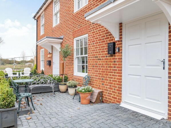 A brick house with a white door, a small patio with outdoor furniture, and potted plants.