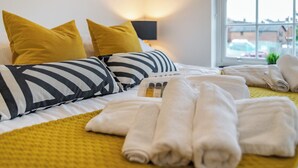 Un lit bien fait, agrémenté d’oreillers à rayures, d’une couverture jaune et de serviettes enroulées, le tout posé sur un couvre-lit jaune.
