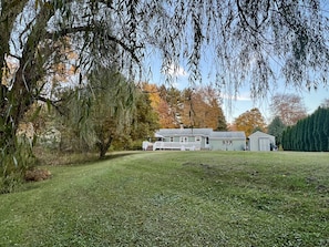 Ein Haus mit Veranda, einer kleinen Gartenhütte und einem gepflegten Rasen.