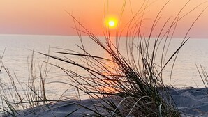 A sunset over a beach with sand and grass in the foreground.