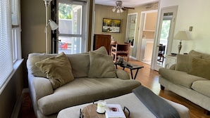 A living room with two striped sofas, a wooden coffee table with a book and candle, and a TV on the wall.