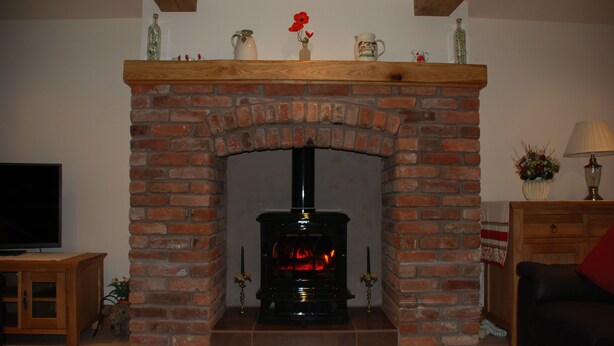 A brick fireplace with a black stove, a wooden mantel, and a television on a wooden cabinet to the left.