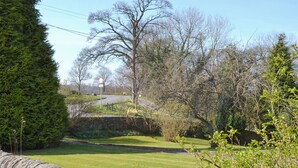 A rural road with a stone wall, trees, and a clear sky.