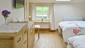 A bedroom with a wooden dresser, a chair, a bed with floral bedding, a radiator, a window with curtains, and a skylight.