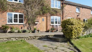 A two-story brick house with a stone pathway leading to the front door, surrounded by potted plants and a small garden.