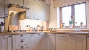 Une cuisine avec des meubles gris, une cuisinière à gaz, un grille-pain et une fenêtre donnant sur l’extérieur.