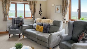 Un salon chaleureux avec un canapé gris, un fauteuil assorti et une petite table basse en bois sur laquelle est posée une plante.