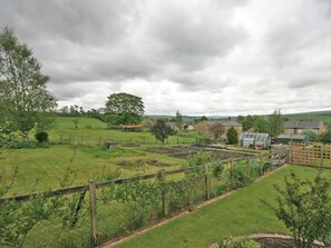 A rural landscape with a fenced garden area, a greenhouse, and a variety of trees and buildings in the background.
