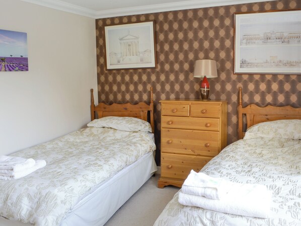 A bedroom with two single beds, a wooden dresser, and a lamp.