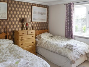 A bedroom with two beds, a dresser, a lamp, and a window with curtains.