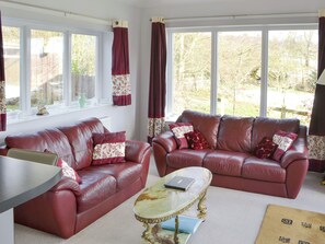 A living room with two red leather sofas, a glass coffee table, and large windows with curtains.