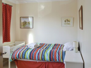 A bedroom with a bed, a crib, a nightstand, and two framed pictures on the wall.