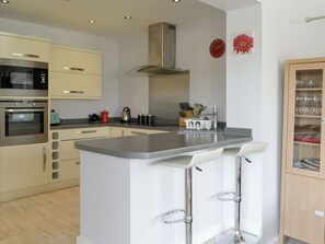 A modern kitchen with stainless steel appliances, a central island with bar stools, and a wooden cabinet with glassware.