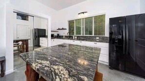 Eine moderne Küche mit weißen Schränken, einer Arbeitsplatte aus Granit, einem schwarzen Kühlschrank und einem Fenster mit Jalousien.