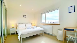 A bedroom with a bed, bedside tables, a window, a radiator, a desk, and a chair.