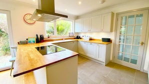 A modern kitchen with a central island, white cabinetry, a large window, and a view of greenery.