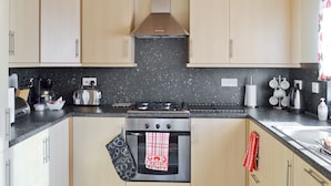 Een moderne keuken met lichte houten kastjes, een zwart granieten aanrecht en een rvs-fornuis met een inbouwoven.