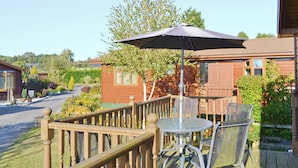 Een houten terras met een tafel, stoelen en een parasol, met uitzicht op een woonwijk met huizen en bomen.