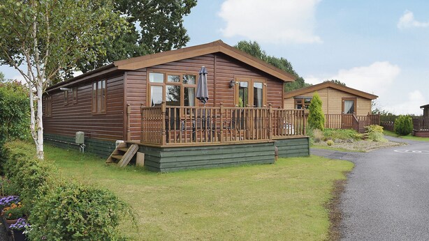 Een houten chalet met een veranda, omgeven door een tuin vol verschillende bloemen.