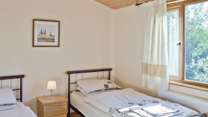Een slaapkamer met twee bedden, een nachtkastje met een lamp, een lijst met een afbeelding aan de muur en een raam met gordijnen.