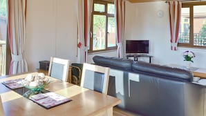 Een woonkamer met een bank, een televisie en een eettafel met stoelen.