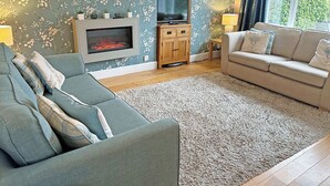 A living room with a sofa, a TV, a fireplace, and a window. - 2 bedroom accommodation in Lamlash, Isle of Arran (Lamlash, Isle of Arran)