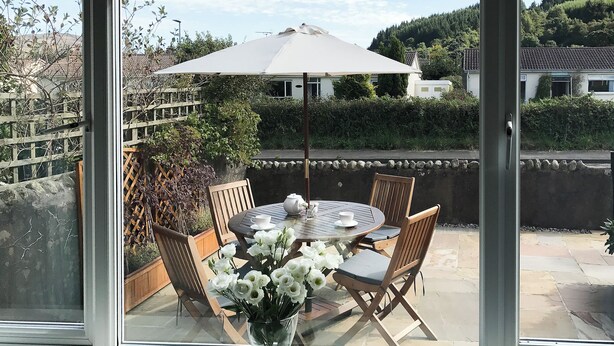 A patio with a table, chairs, a white umbrella, and a vase with white flowers. - 2 bedroom accommodation in Lamlash, Isle of Arran (Lamlash, Isle of Arran)