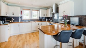 A modern kitchen with white cabinets, a wooden countertop, and a built-in stove. There are two windows with blinds, a stainless steel range hood, and a small TV on the counter. - 3 bedroom accommodation in Port Lamont near Dunoon (Port Lamont near Dunoon)