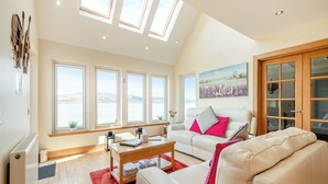 A spacious living room with a high ceiling, large windows, a white sofa, a coffee table, and a painting on the wall. - 3 bedroom accommodation in Port Lamont near Dunoon (Port Lamont near Dunoon)
