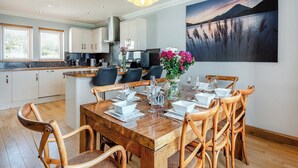 A modern kitchen with white cabinets, a wooden dining table set for six, and a large painting of a landscape on the wall. - 3 bedroom accommodation in Port Lamont near Dunoon (Port Lamont near Dunoon)