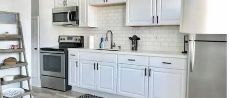 A modern kitchen with white cabinets, stainless steel appliances, and a wooden ladder shelf.