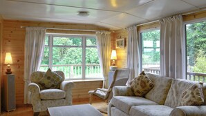 A cozy room with wooden walls, two armchairs with floral upholstery, a sofa with patterned cushions, a wooden coffee table, and a window with curtains. - 2 bedroom accommodation in Nairn, Morayshire (Nairn, Morayshire)