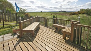 A wooden deck with benches overlooking a grassy field and a blue flag. - 2 bedroom accommodation in Nairn, Morayshire (Nairn, Morayshire)