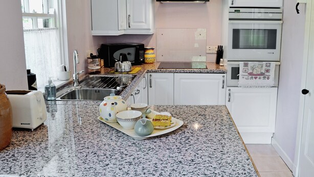 A kitchen with white cabinets, a black microwave, a stove, and a sink.