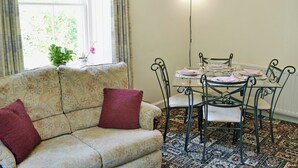 A dining area with a table set for four, surrounded by four chairs, a sofa with two cushions, and a window with curtains.